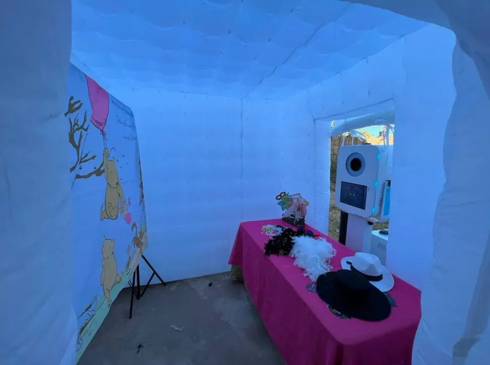 Inside the inflatable photo booth: printed backdrop, props table with hats and boas, and the booth ready to shoot